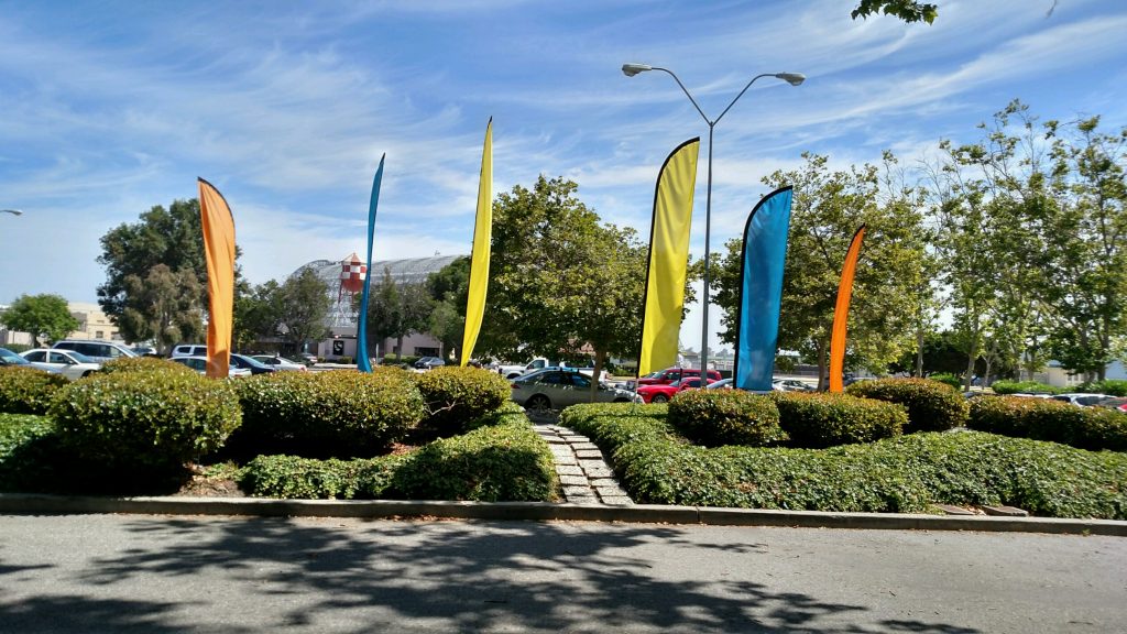 A group of brightly colored feather flags around a parking lot
