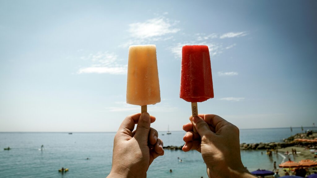 Holding two popsicles side by side at the beach